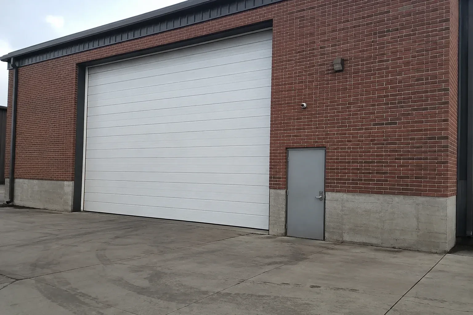 Tall closed sectional loading door beside a personnel door at a brick unit. — Commercial Sectional Door Repair, Waterloo